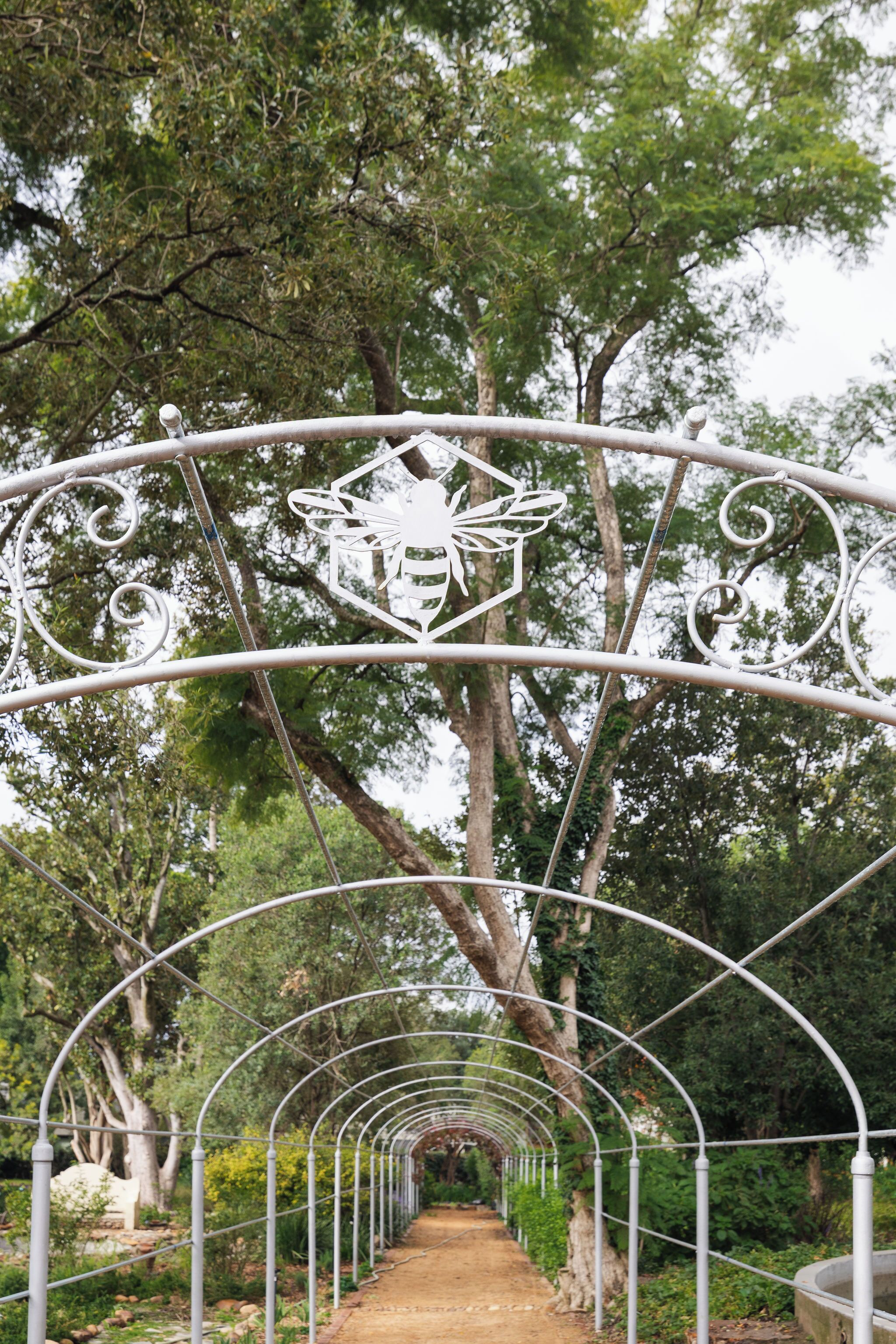 A metal pathway with a decorative archway featuring a bee design, surrounded by trees.
