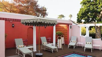Zona de piscina con sillones de descanso, una pérgola y una pared roja.