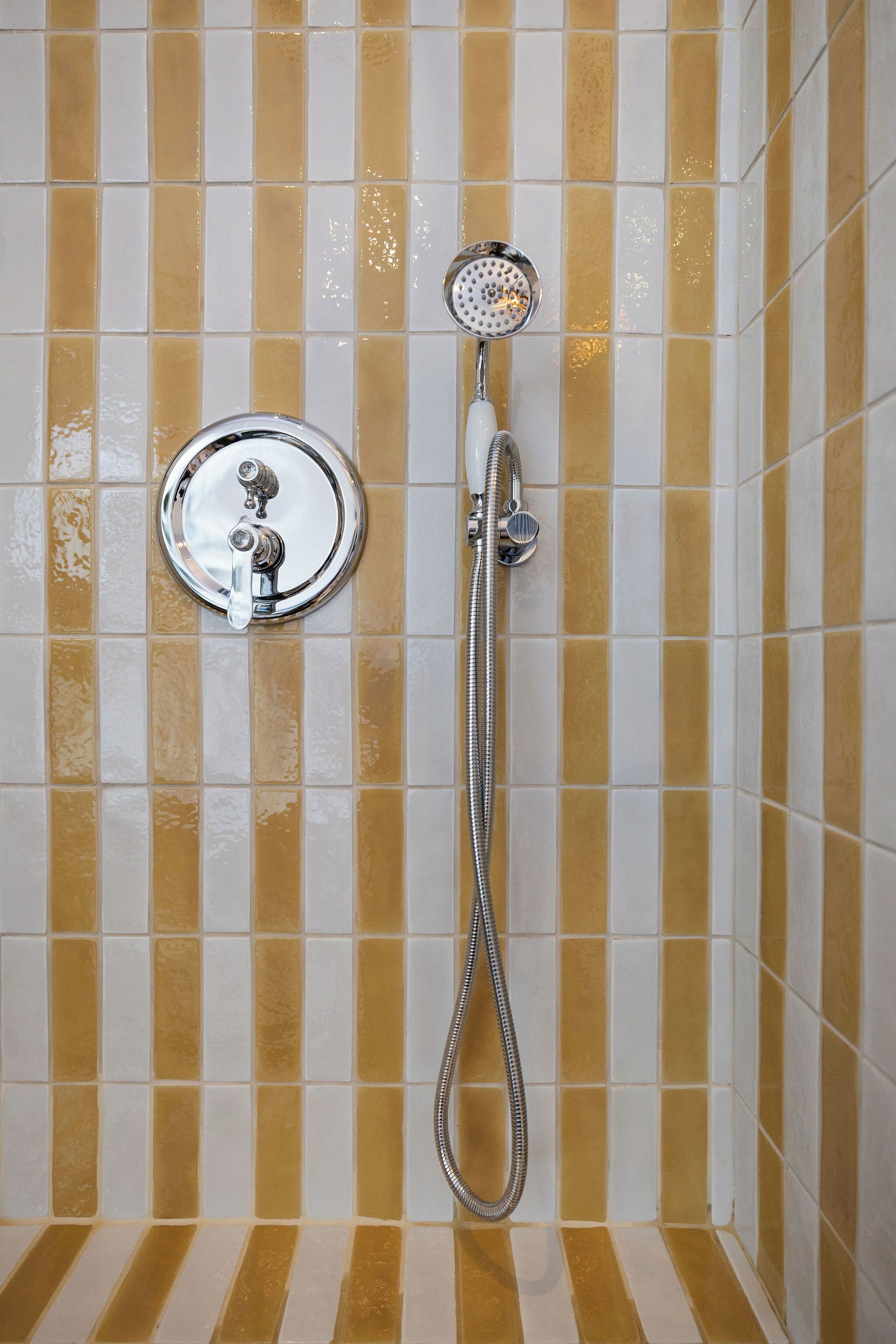 Zona de ducha con cabezal de ducha manual y llave de control en la pared.