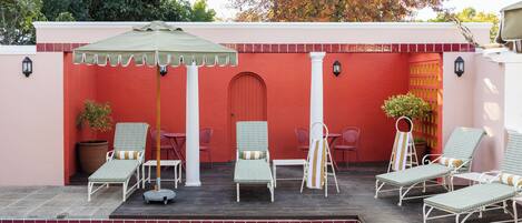 A poolside area with lounge chairs, a table, and a covered seating area.