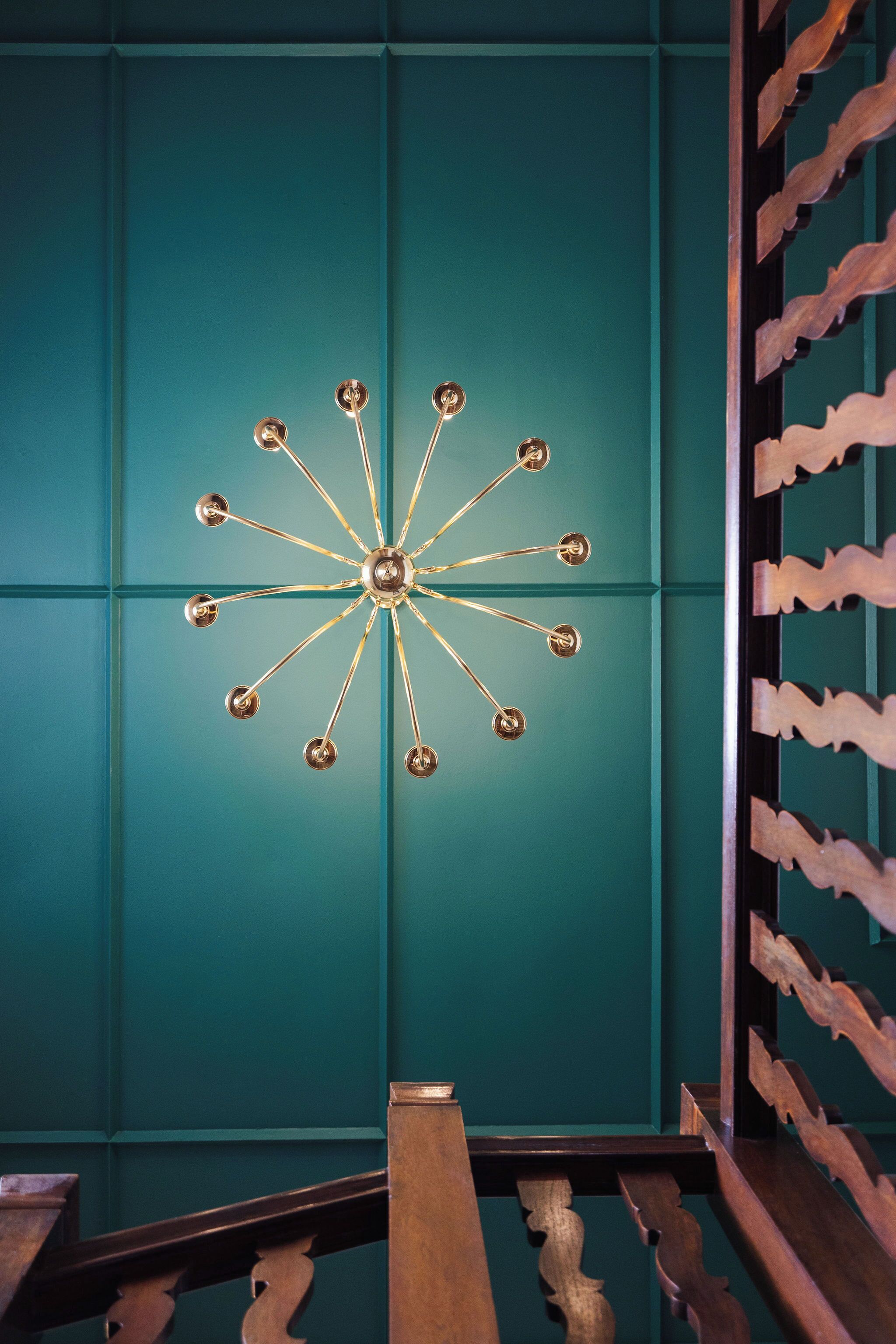 Una pared color turquesa con una lámpara de techo tipo estrella y una escalera de madera con barandillas ornamentadas.