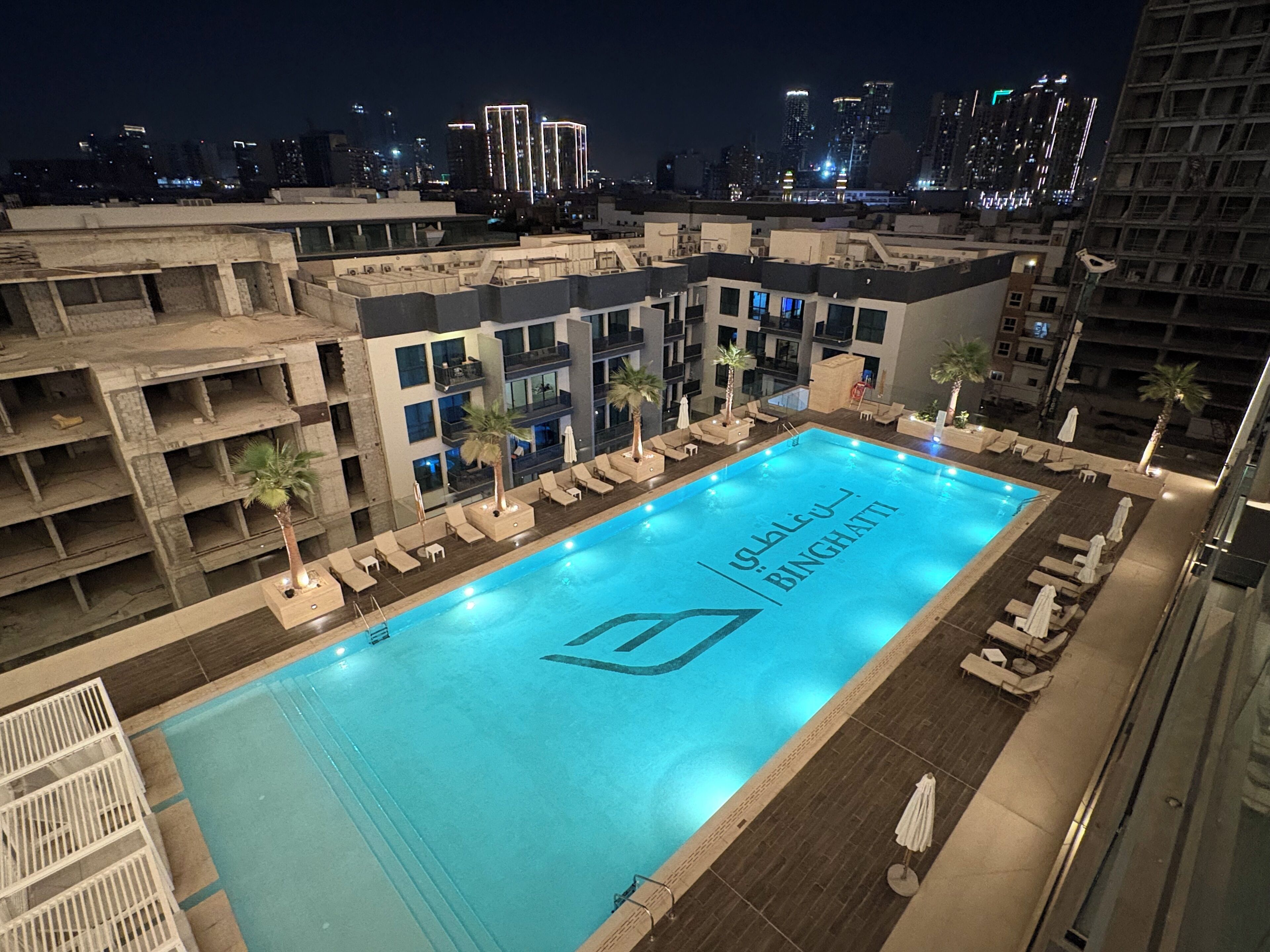 Piscina en la azotea con vista al horizonte de una ciudad de noche.