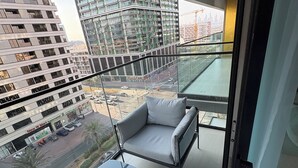 A balcony with a sofa and table, overlooking a cityscape with modern buildings and a road. - Luxury 2BR Apartment Dubai, Pool, Gym & Free Parking (Dubai)