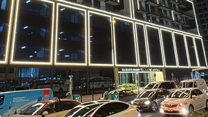 A multi-story building with illuminated lines on the facade, a parking lot with cars, and a sign for 'GIATTI ORCHIDS'. - Luxury 2BR Apartment Dubai, Pool, Gym & Free Parking (Dubai)