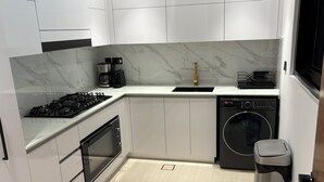 A modern kitchen with white cabinets, a built-in oven, a gas stove, a coffee maker, a dishwasher, and a trash bin. - Luxury 2BR Apartment Dubai, Pool, Gym & Free Parking (Dubai)