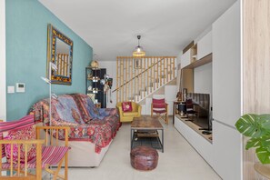 Ein Wohnzimmer mit einer Couch, Sesseln, einem Couchtisch, einem Fernseher und einer Treppe.
