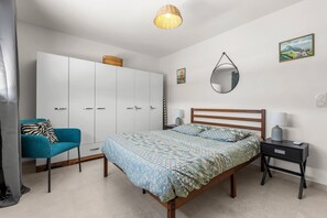 Une chambre à coucher comprenant un lit, une chaise, une armoire, une table de chevet, une lampe, un miroir et un tableau accroché au mur.
