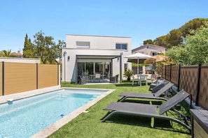 A modern outdoor pool area with a clear blue pool, a wooden fence, and a lounge area with chairs. - Villa La rose des vents by Sur la mer (Saint-Aygulf)