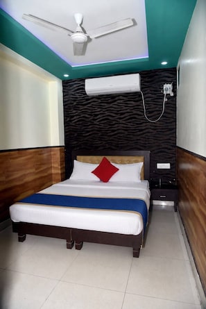 Un dormitorio con cama, ventilador de techo, aire acondicionado y mesita de noche.