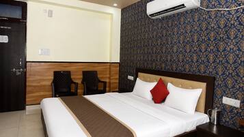 Habitación de hotel con cama, dos sillas, equipo de aire acondicionado, mesita de noche y pared con diseño.