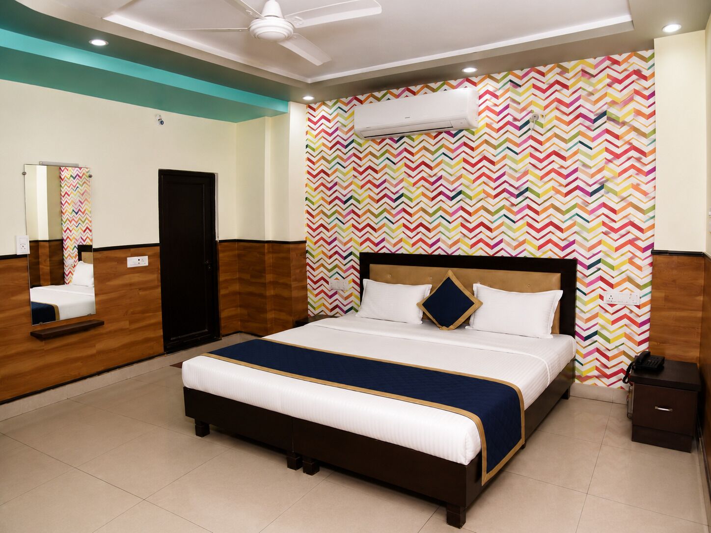 Una habitación de hotel con una cama grande, un espejo, un armario y un ventilador de techo.