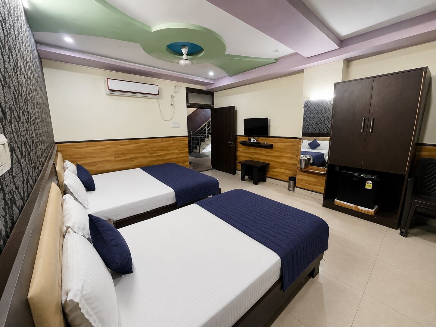 Habitación de hotel con dos camas, un televisor, un escritorio, un armario y un ventilador de techo.