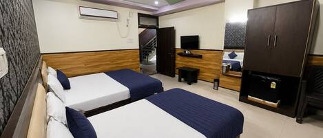 A hotel room with two beds, a TV, a desk, a wardrobe, and a ceiling fan.