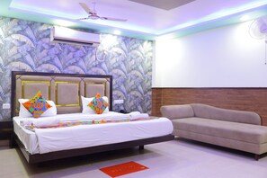 A hotel room with a bed, a sofa, a ceiling fan, and a wall-mounted air conditioner. - Hotel Sumangal (Gwalior)