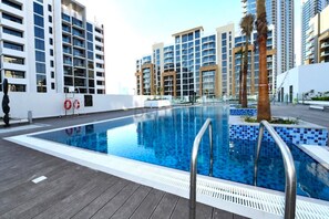 Ein moderner Pool mit Holzterrasse, umgeben von Hochhäusern.