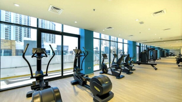 Ein Fitnessstudio mit Cardiogeräten, Krafttrainingsgeräten und großen Fenstern mit Blick auf die Stadt.