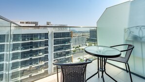 Ein Balkon mit einem Glastisch und zwei Stühlen, mit Blick auf eine Skyline moderner Gebäude.