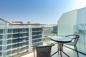 Ein Balkon mit einem Glastisch und zwei Stühlen, mit Blick auf eine Skyline moderner Gebäude.