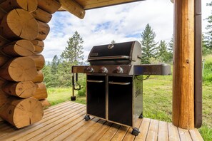 Ein Genesis tragbarer Grill auf einer Holzterrasse vor Bäumen und einem klaren Himmel.