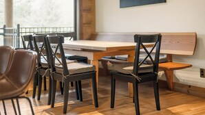 Uma área de refeições com mesa e cadeiras de madeira, um banco e vista para o exterior.