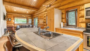 Interior de cabana de madeira com ilha na cozinha, armários de madeira e área de jantar.