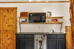Uma cozinha compacta com micro-ondas, cafeteira e um violino em uma prateleira.