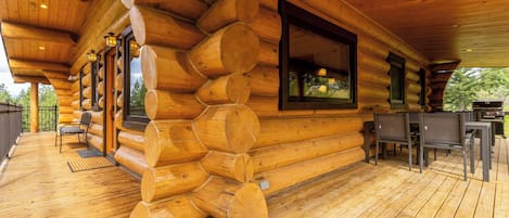 A log cabin with a wooden deck, outdoor seating, and a large window overlooking the outdoors.