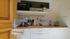 Een keuken met witte kastjes, een houten aanrecht, een zwarte magnetron en een 'Willkommen' bord.