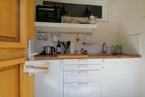 Eine Küche mit weißen Schränken, einer Holz Arbeitsplatte, einer schwarzen Mikrowelle und einem 'Willkommen' Schild.