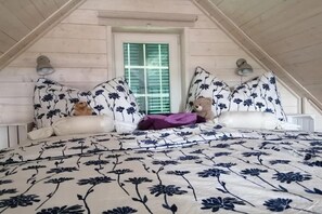 Ein Schlafzimmer mit schrägen Wänden, einem Fenster mit Rollläden, zwei Wandleuchten und einem Bett mit Blumenmuster auf der Bettwäsche.