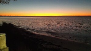 Ein Sonnenuntergang über ruhigem Gewässer mit Sandstrand und einer Holzkonstruktion.