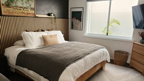 Ein Schlafzimmer mit einem Bett, einem Fenster mit Blick, einem Nachttisch und einem an der Wand befestigten Regal.
