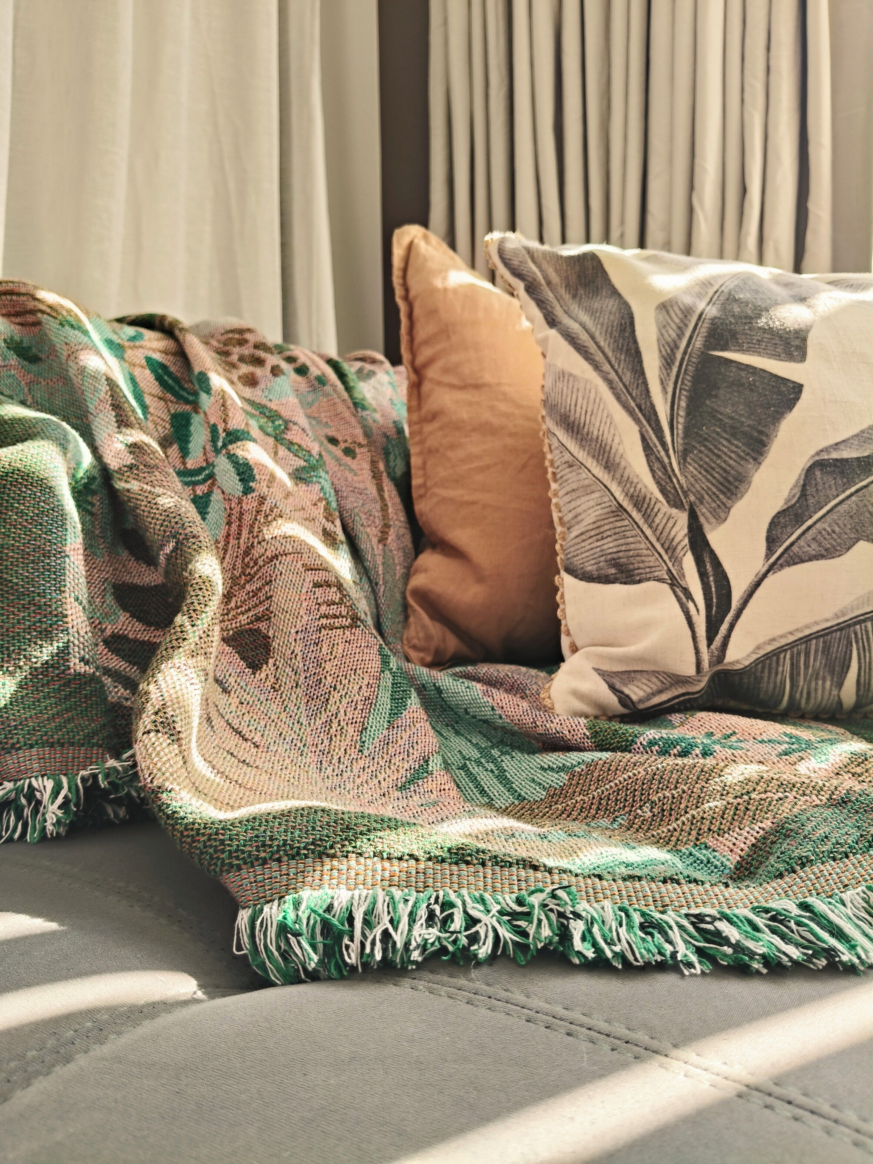 A bed with a patterned blanket and pillows, a window with curtains, and a view of the outside.