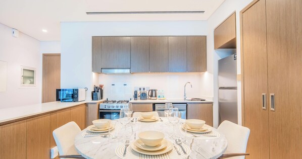 A modern kitchen with a dining area, featuring a marble table, wooden cabinets, and stainless steel appliances. - Cozy 1BR near Burj Khalifa, Downtown (Downtown)
