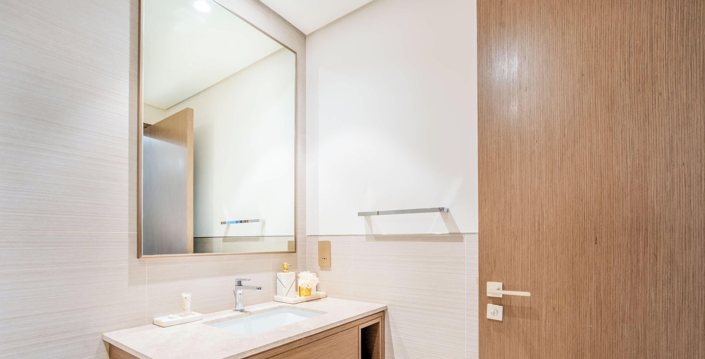 A bathroom with a large mirror, a sink, and a wooden door.