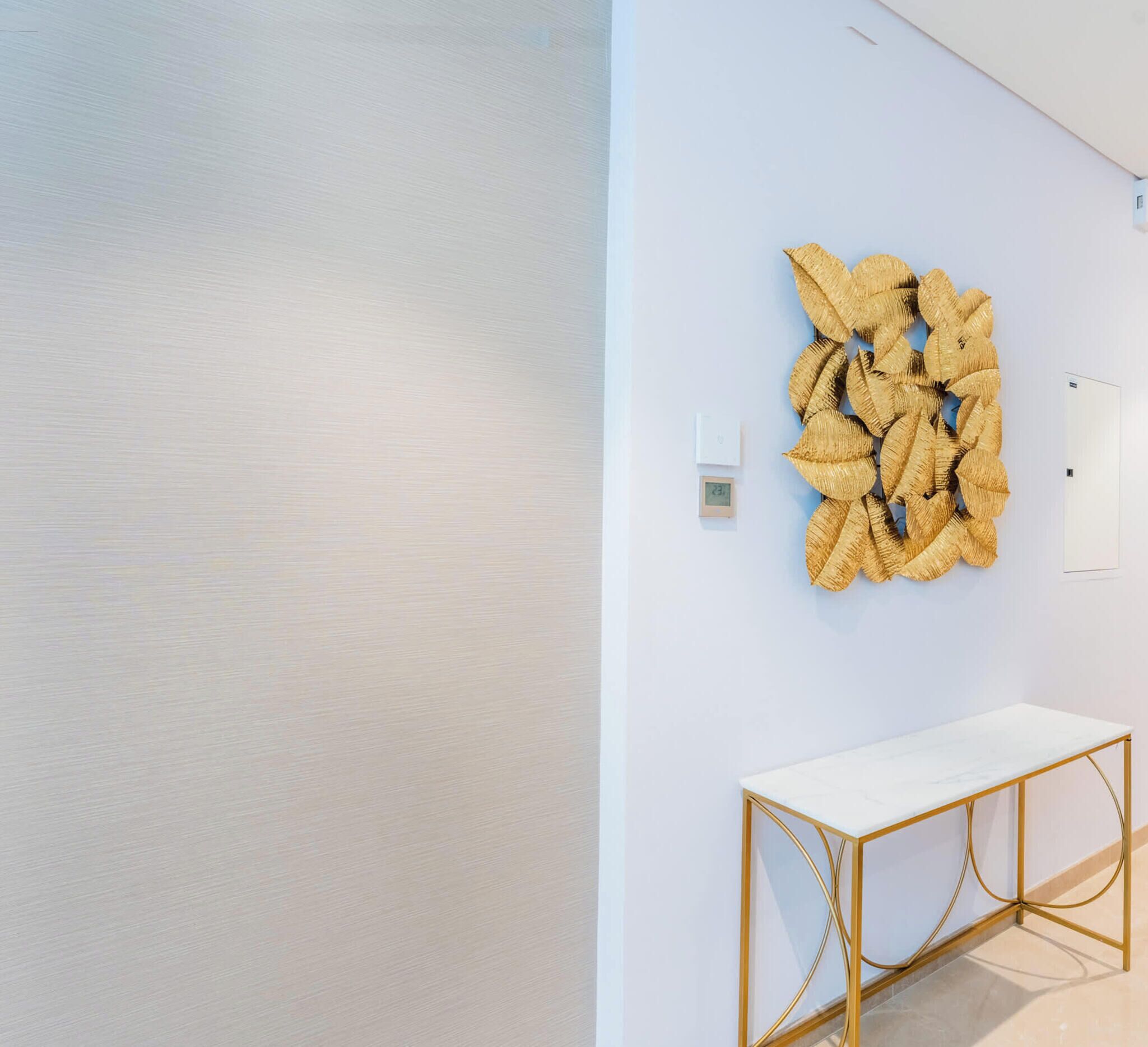 Un interno minimalista con un muro bianco, un tavolo consolle con cornice dorata e un'opera d'arte con texture sulla parete.
