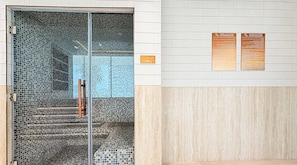 A steam room with tiled walls and a glass door, and two informational signs on the wall. - Modern 1BR, Binghatti Royale, JVC (Dubai)