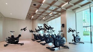 A gym with multiple stationary bikes arranged in rows, large windows, and a high ceiling with recessed lighting. - Modern 1BR, Binghatti Royale, JVC (Dubai)