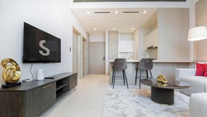A modern living room with a flat-screen TV, a dark wood entertainment unit, a round coffee table, and a sofa with red cushions. - Modern 1BR, Binghatti Royale, JVC (Dubai)