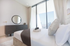 A modern bedroom with a large bed, a bedside table, a mirror, and a view of the city through floor-to-ceiling windows. - Modern 1BR, Binghatti Royale, JVC (Dubai)