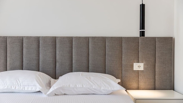 Ein Bett mit grauem Polsterkopfteil, weißer Bettwäsche und einem Nachttisch mit Lampe.