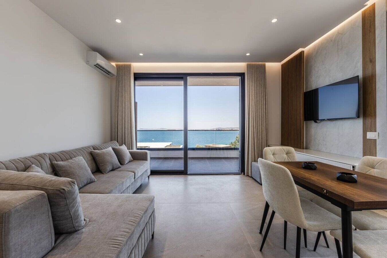 A modern living room with a sofa, a dining table, and a TV mounted on the wall.