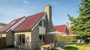 Une maison avec un toit recouvert de tuiles rouges, une cheminée en briques et une terrasse avec une table et des chaises.