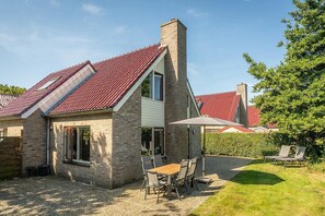 Ein Haus mit rotem Ziegeldach, einem Backstein-Schornstein und einer Terrasse mit Tisch und Stühlen.