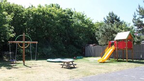 Une aire de jeux avec des balançoires, un toboggan et une table de pique-nique.