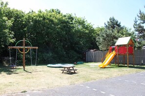 Ein Spielplatz mit Schaukeln, einer Rutsche und einem Picknicktisch.