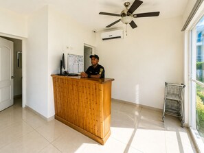 Ein Empfangsschalter mit Deckenventilator, Klimaanlage, einem Computermonitor und einem Fenster mit Blick ins Grüne.