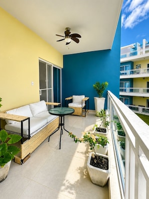 Ein Balkon mit einer Couch, einem Tisch, Stühlen, Topfpflanzen und einem Deckenventilator.