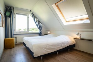 A bedroom with a bed, a window, a skylight, a bedside table with a lamp, and a radiator. - Texel Getaway with Whirlpool (De Koog)