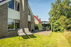 A two-story house with a brick exterior, a red roof, and a patio area with a table and chairs. - Texel Getaway with Whirlpool (De Koog)